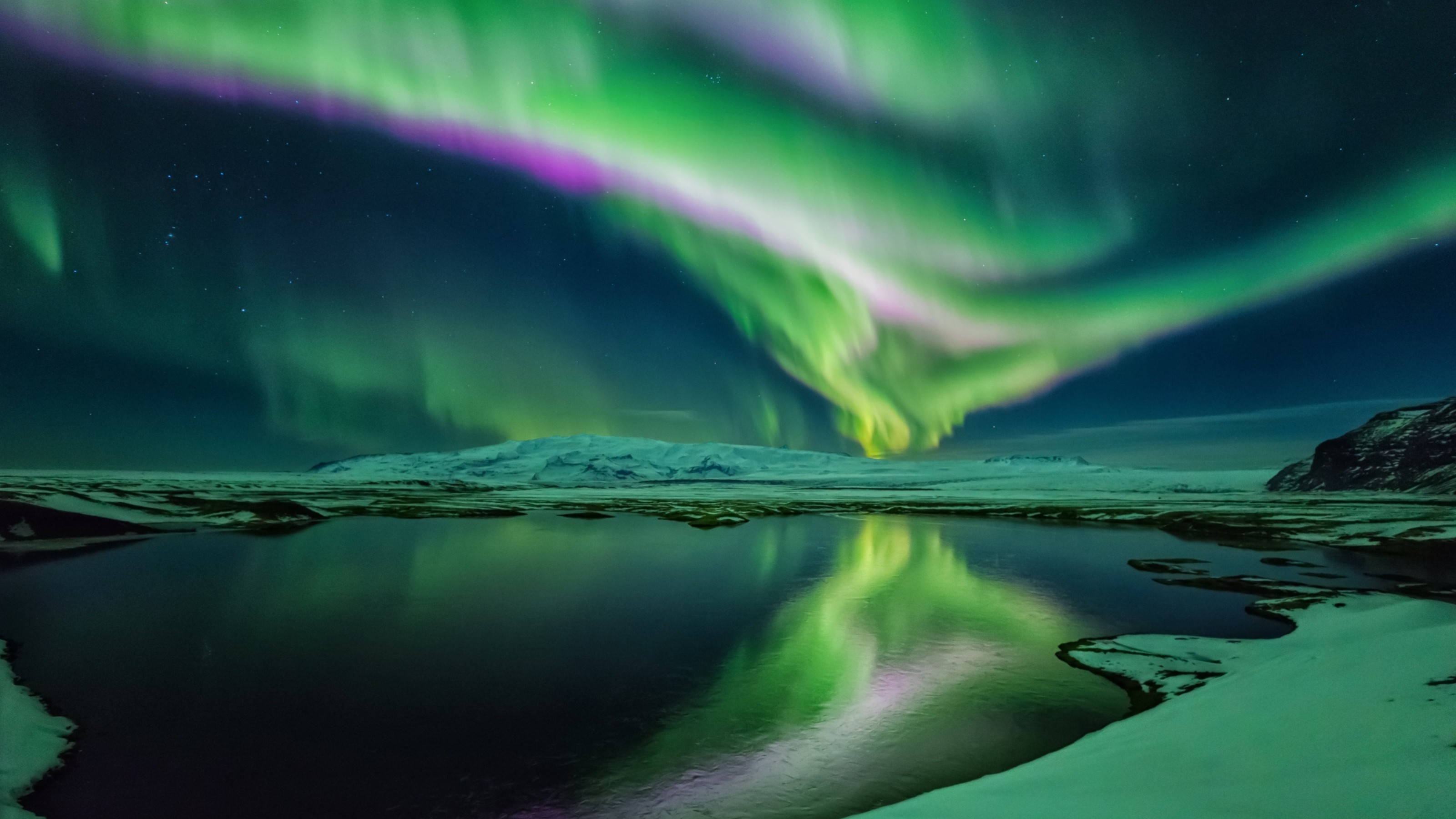 Aurora borealis dancing over a snowy landscape with reflection in the water.