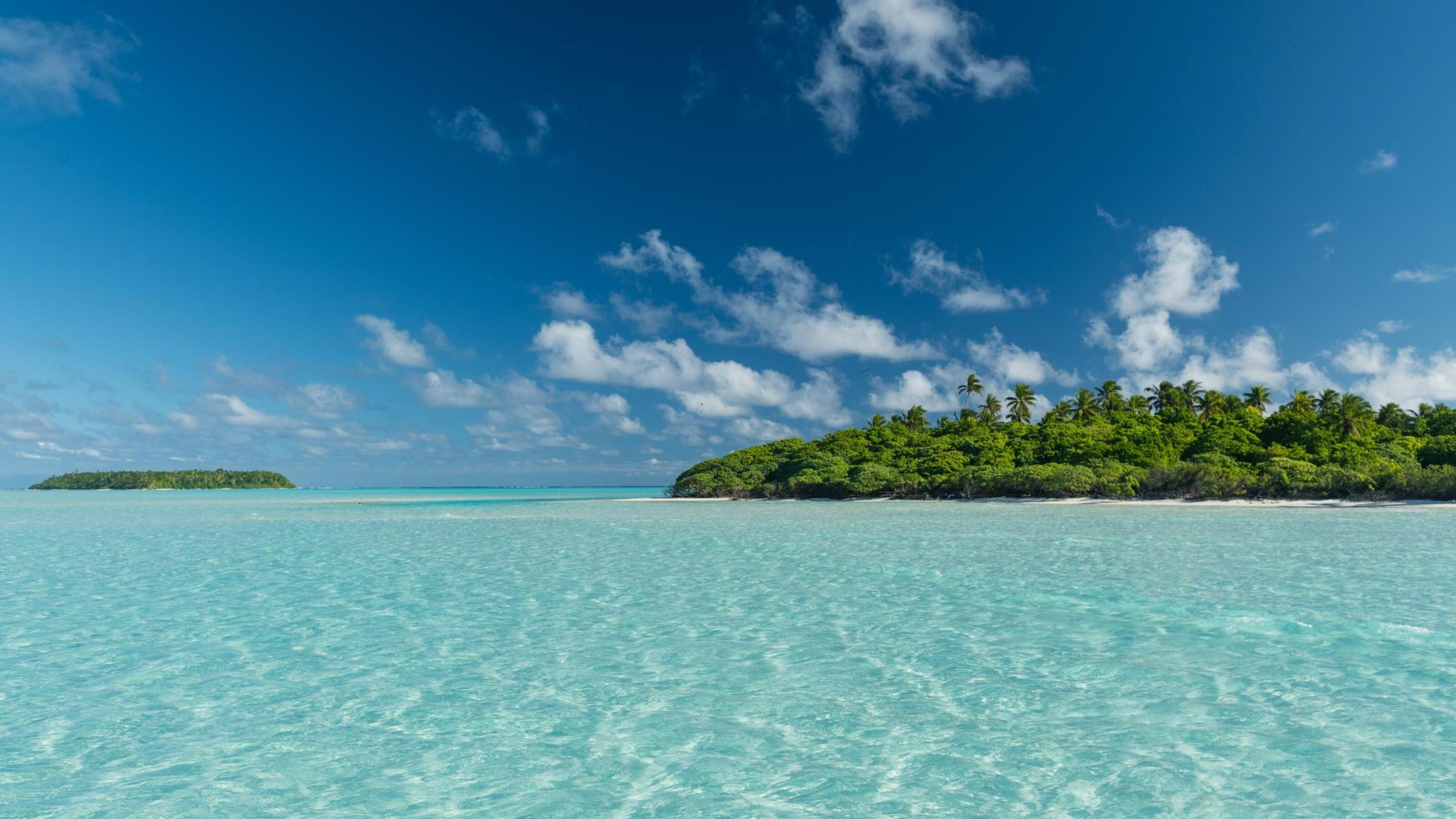Tropical paradise with clear turquoise water, lush green islands, and blue sky with clouds.