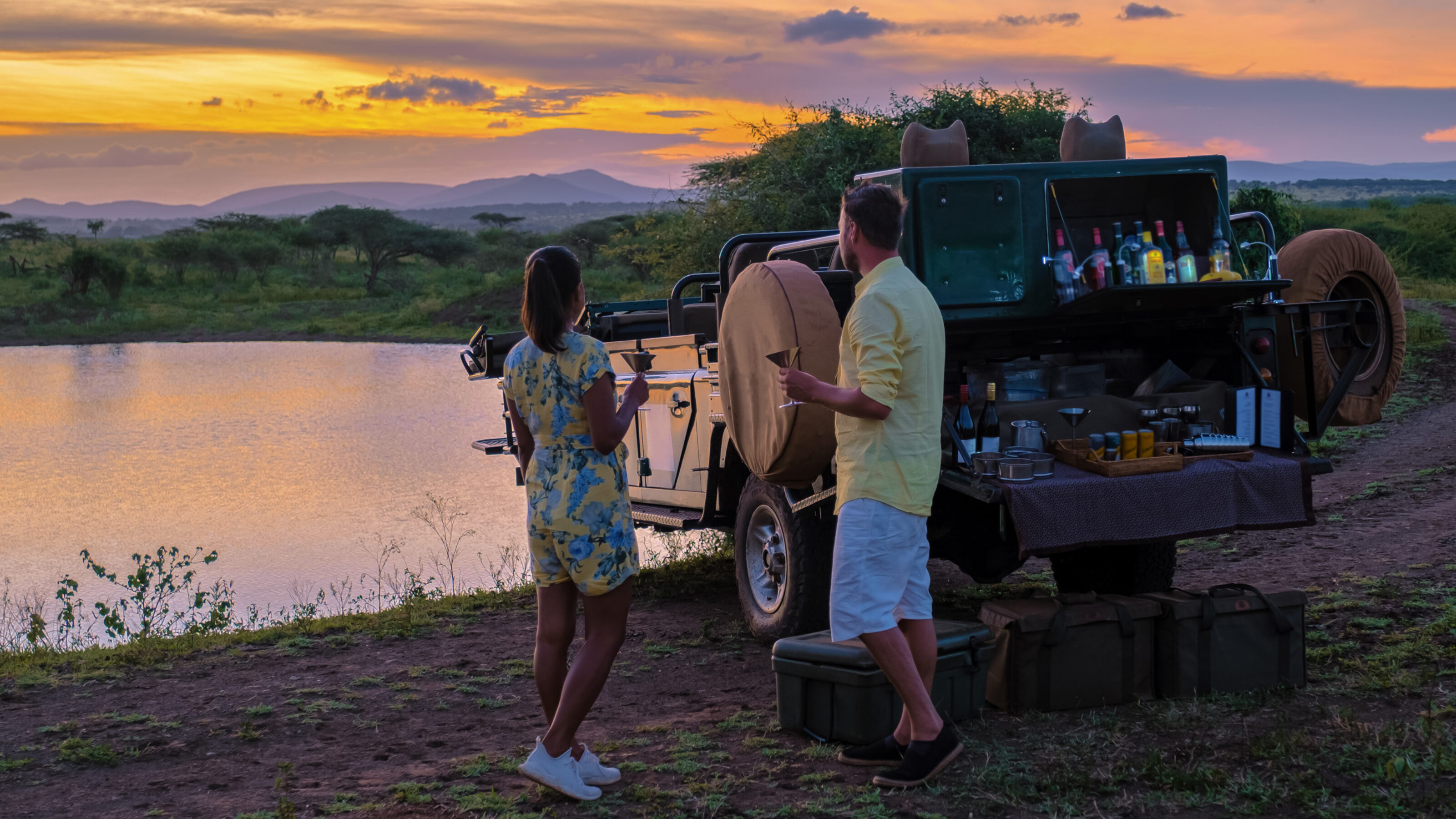 A couple of men and an Asian woman on safari in South Africa, a luxury safari car during a game drive, couple men and woman on safari in South Africa at sunset sundowner with cocktails and drinks