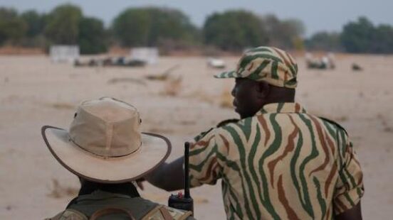 Two people in safari attire observing an open area.