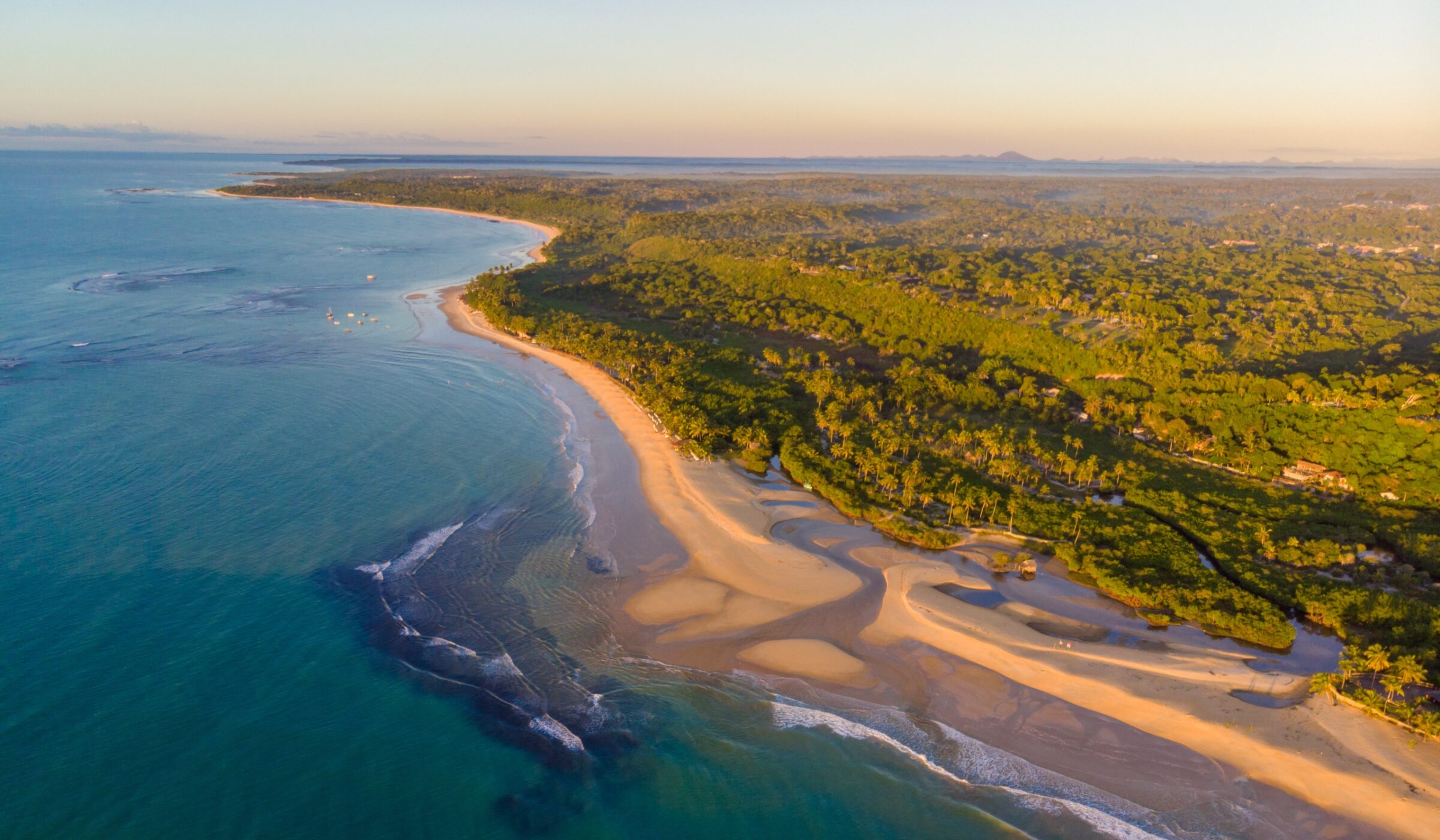 Aerial view of a sunlit coastline with beach, sea, and dense greenery.