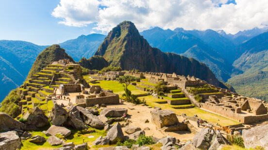 Sunny view of Machu Picchu ruins with Huayna Picchu mountain in the background.