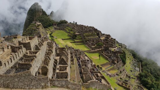 Machu Picchu ruins with tourists and misty mountains in the background.