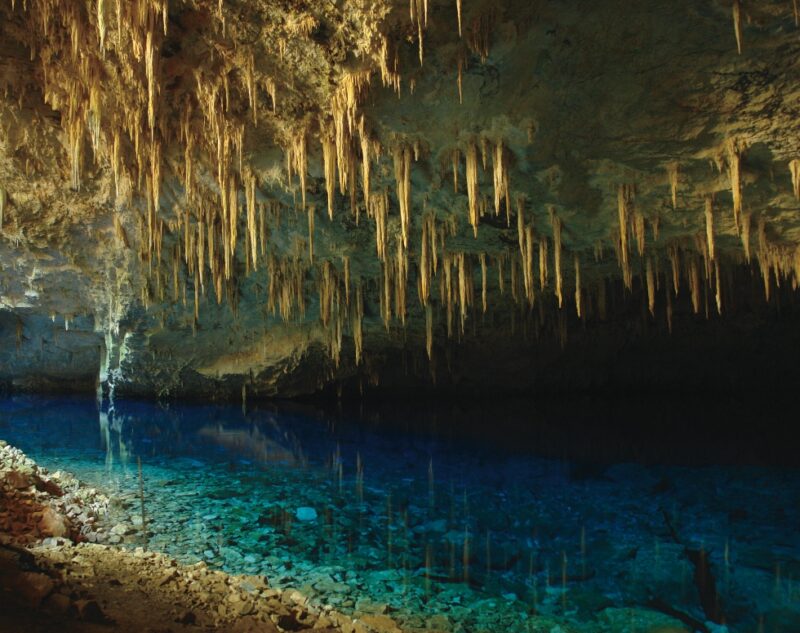 Interior of a cave with many stalactites hanging over clear blue water on luxury Pantanal vacations.