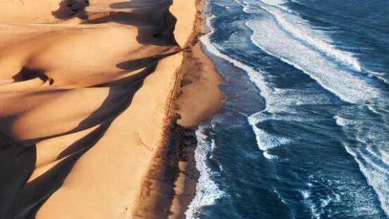 Aerial view of a coastline where vast sand dunes meet the ocean waves.