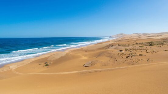 Coastline with vast sand dunes meeting the ocean under a clear blue sky.