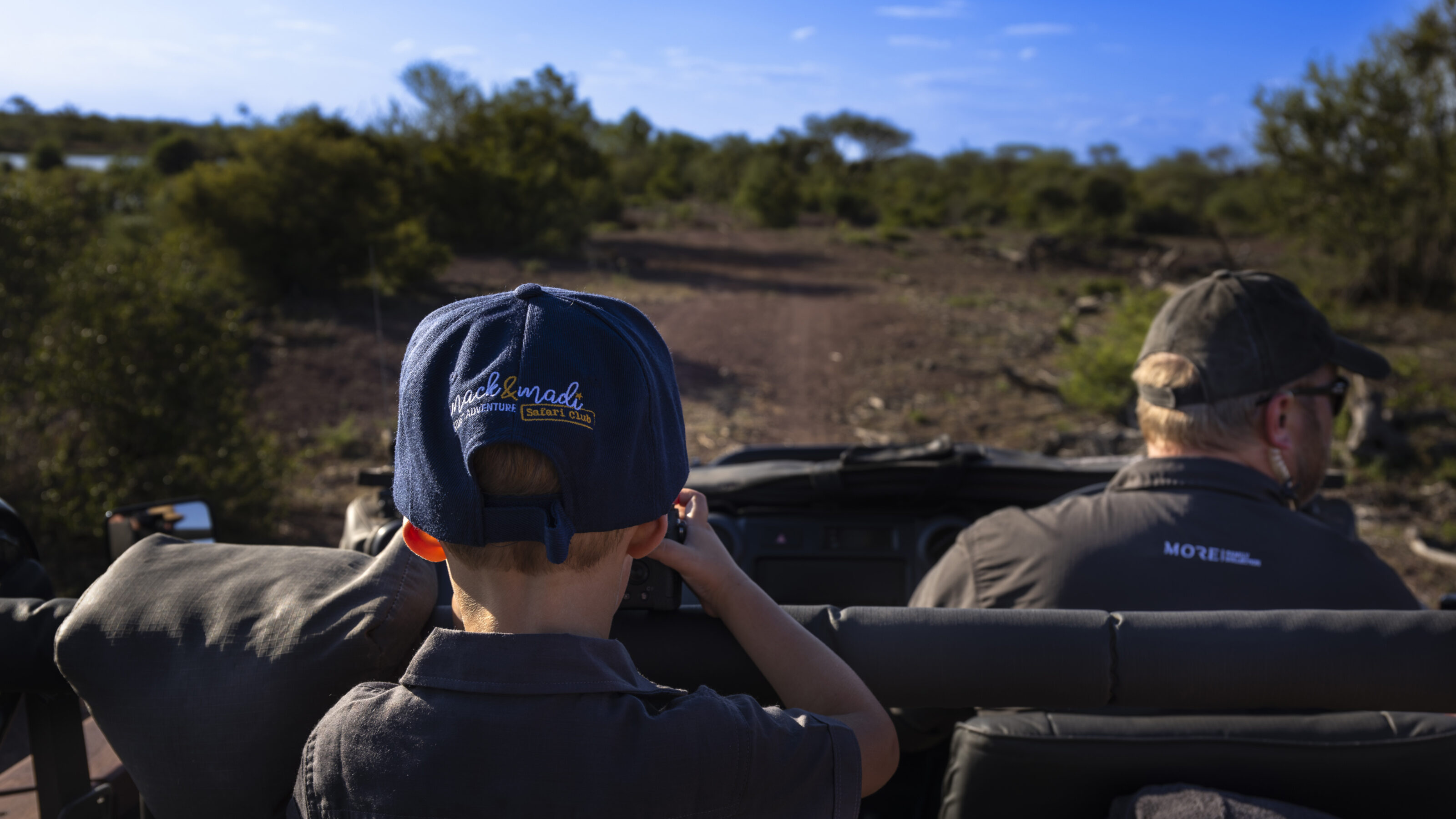 Two people in a safari vehicle observing nature, one wearing a blue cap.