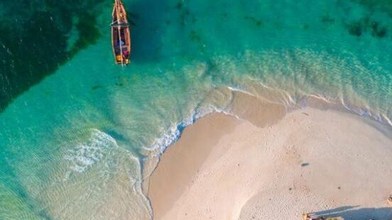 Aerial view of a small boat near a sandy beach jutting into clear, turquoise waters.