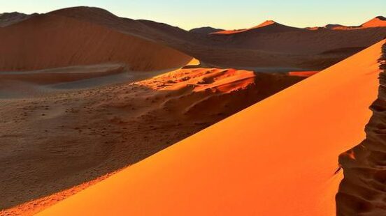 Orange sand dune ridge at sunrise with contrasting shadows in a desert.