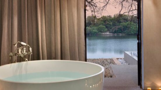 Modern bathroom interior with a round bathtub, warm lighting, and a view of nature through a doorway.