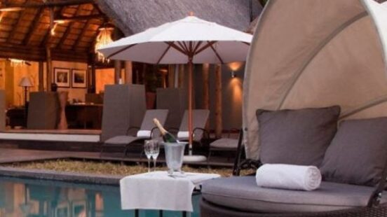Luxury poolside lounge with thatched-roof cabana, sunbeds, umbrella, and champagne.