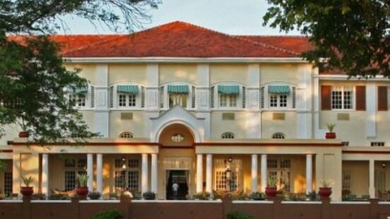 Colonial-style building with red-tiled roof, symmetrical balconies, and illuminated entrance at dusk.