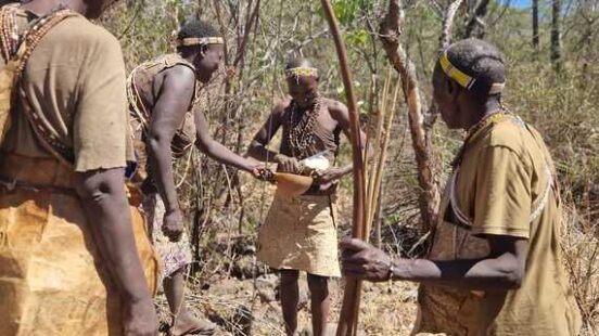 Group of individuals in traditional attire with bows and arrows in a dry, wooded area.