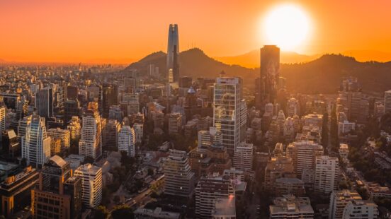 Aerial view of a city skyline at sunset with skyscrapers and mountains in the background.