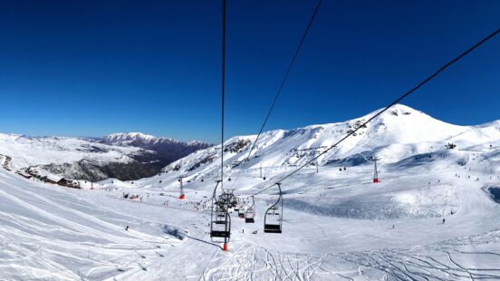 Snow-covered ski slopes with skiers and chairlifts against clear blue sky.
