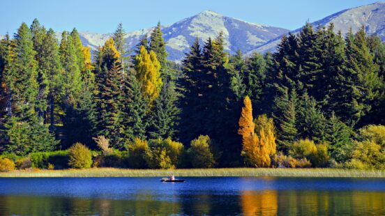 A person kayaking on a calm lake with colorful autumn trees and a mountain backdrop.