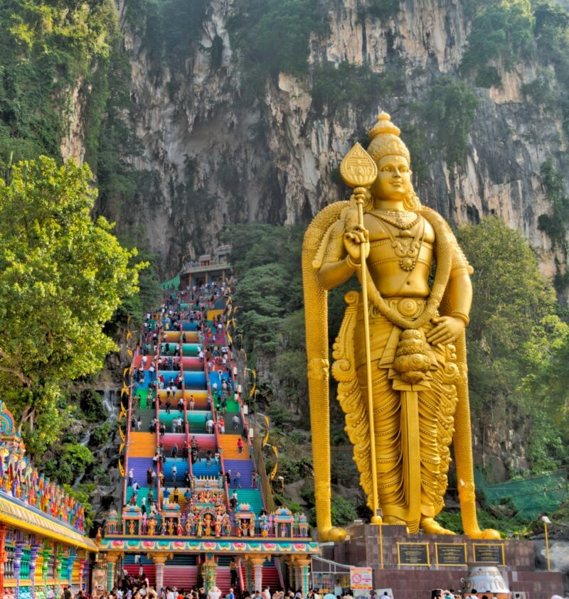 A large golden statue beside colorful steps leading up a limestone cliff.