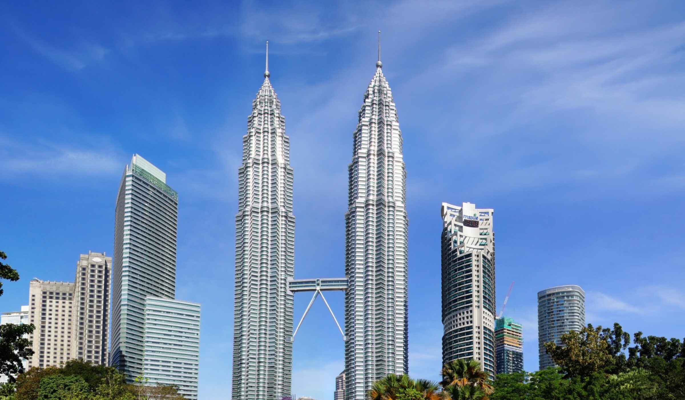 Twin skyscrapers towering above trees against a clear blue sky.