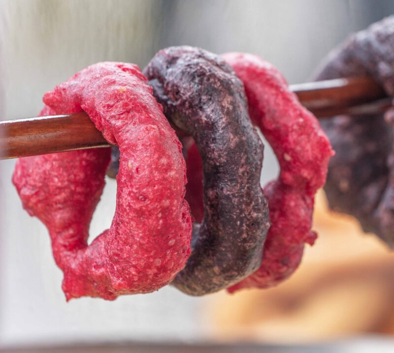 Colorful ring-shaped snacks threaded onto a stick, with a blurry background.