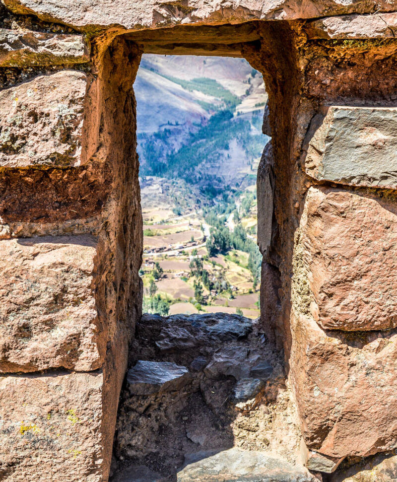A scenic valley viewed through an ancient stone window with clear blue skies above.
