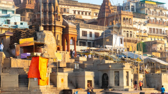 Riverside ghats and temples in Varanasi with reflections on water at sunset.