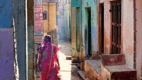 A person walking down a narrow sunlit alley with colorful walls and doors.