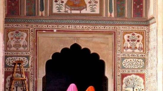 Two women in traditional attire admiring intricate archway designs at an historical building.