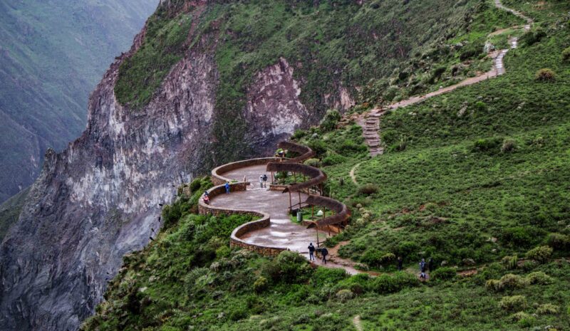 Winding mountain path with pedestrians and verdant slopes.