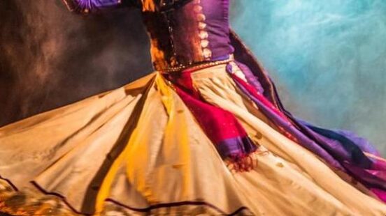 A dancer in traditional attire performing with a twirling skirt on a smoke-illuminated stage.