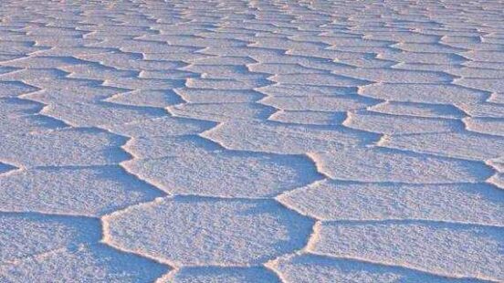 Hexagonal salt flats with a mountain in the distance under a twilight sky.