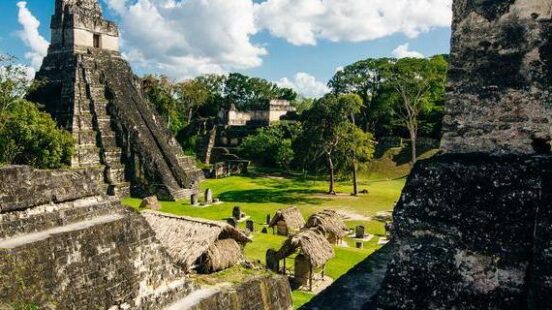 Ancient Maya ruins at Tikal with Temple I in the background under a clear blue sky.