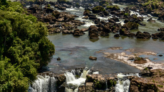 Lush greenery surrounding multiple cascades of a powerful waterfall over rocky cliffs.