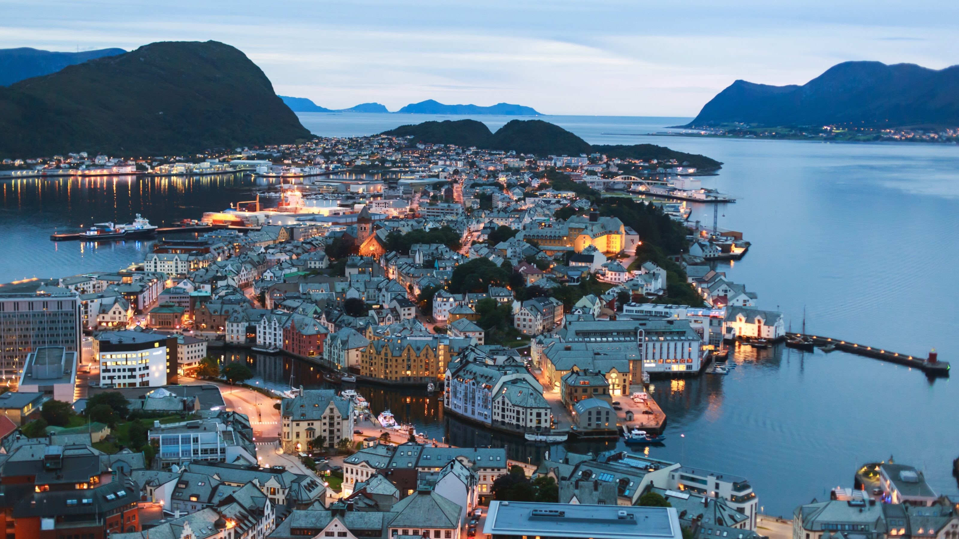 Twilight over a coastal town with lit buildings and calm waters.