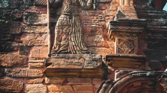 Ancient carved figure on a weathered red brick wall of a historic temple.