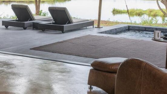 Luxurious outdoor lounging area with chairs overlooking a serene water body and greenery.