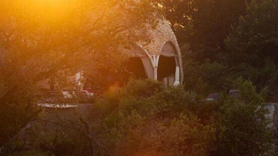 Sunset behind a domed structure by a body of water, with light reflections and trees.