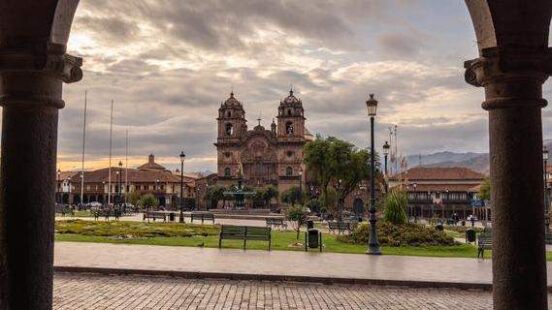 View of a cathedral across a plaza from an arched doorway, with cloudy skies above.