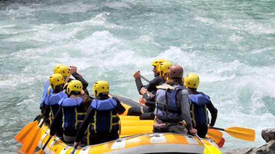 A group in helmets and life jackets whitewater rafting on a turbulent river.