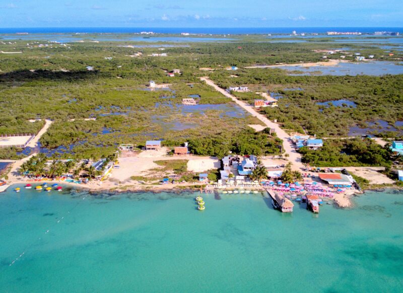 Aerial view of a tropical coastline with turquoise waters, colorful umbrellas, and scattered buildings.