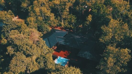 Aerial view of a house with a red roof and pool surrounded by dense, autumn-colored forest.