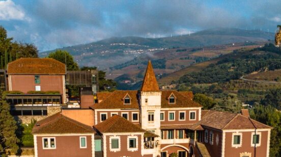 Aerial view of a terracotta-roofed villa with gardens, amidst rolling hills and blue skies.