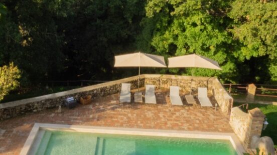 Outdoor pool with sun loungers and umbrellas overlooking green hills.