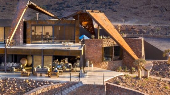Modern desert house with a pool, nestled against a rocky hillside.