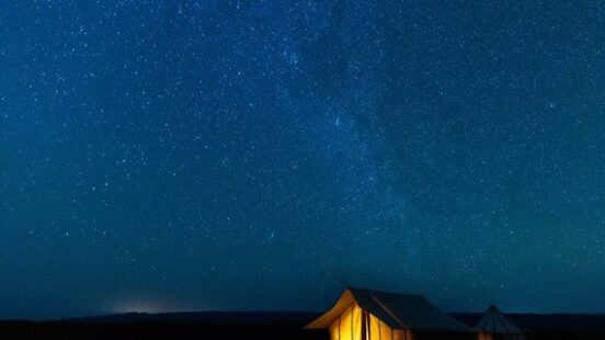 Tent illuminated under a starry night sky.