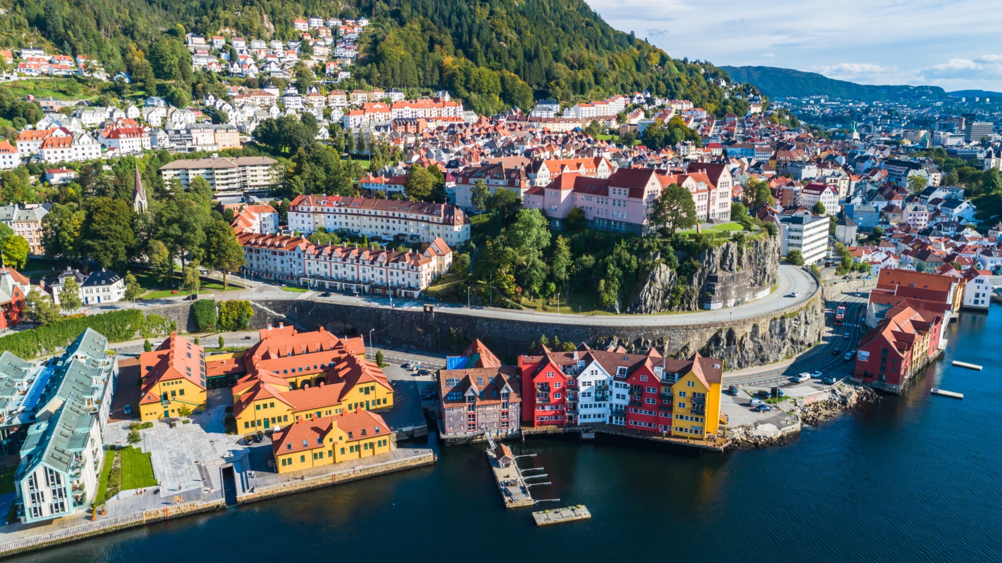 Aerial view of a coastal town with colorful houses by the waterfront and hills in the background.