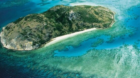 Aerial view of a crescent-shaped island surrounded by turquoise waters and coral reefs.