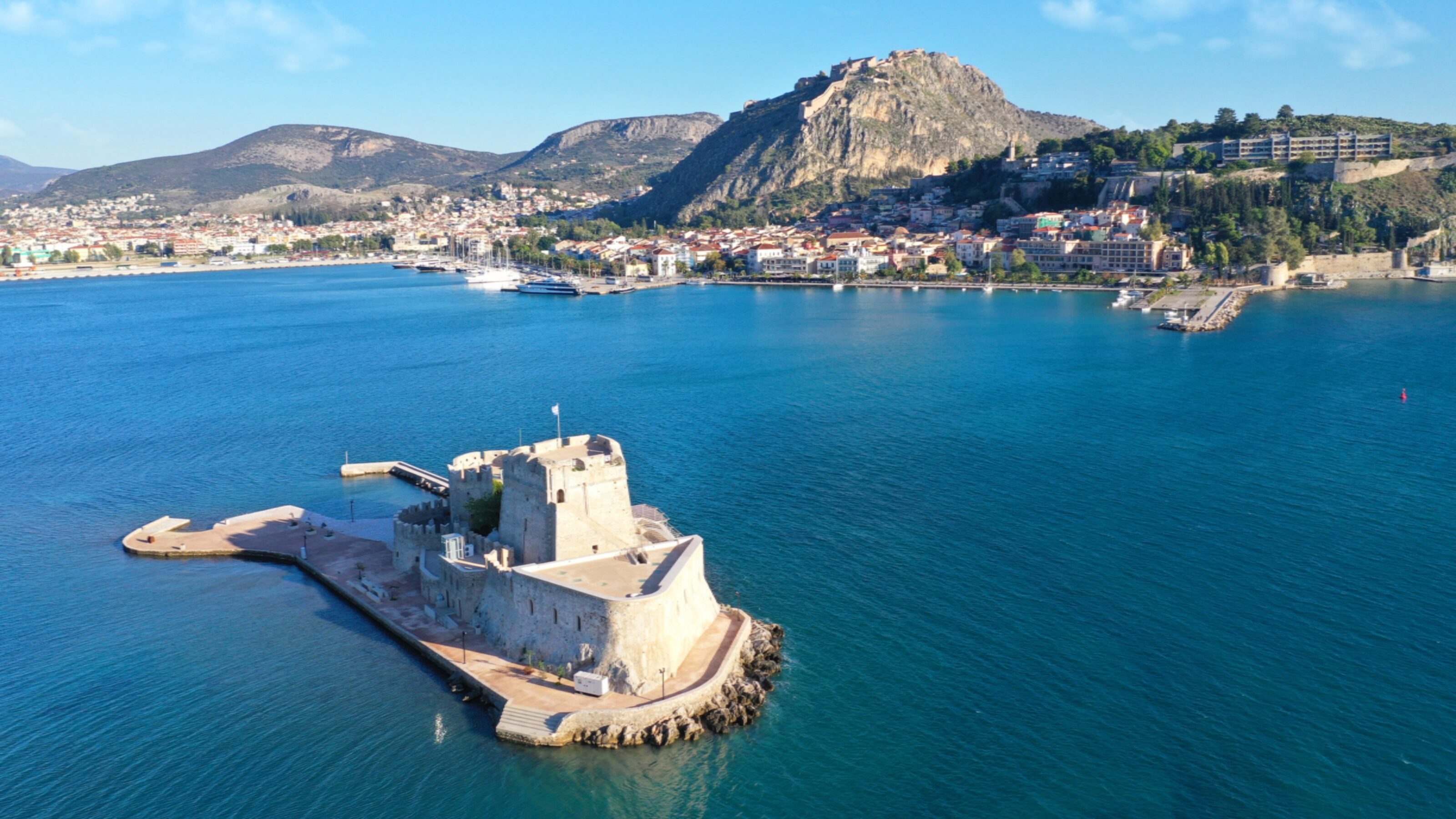 Aerial view of a coastal fortress with hills and a city in the background.