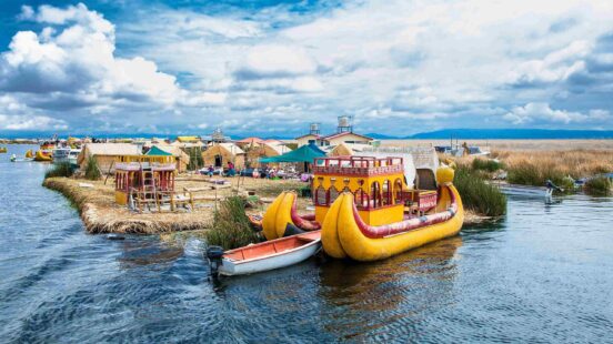 Colorful reed boats and houses on the floating Uros Islands of Lake Titicaca, under a cloudy sky.