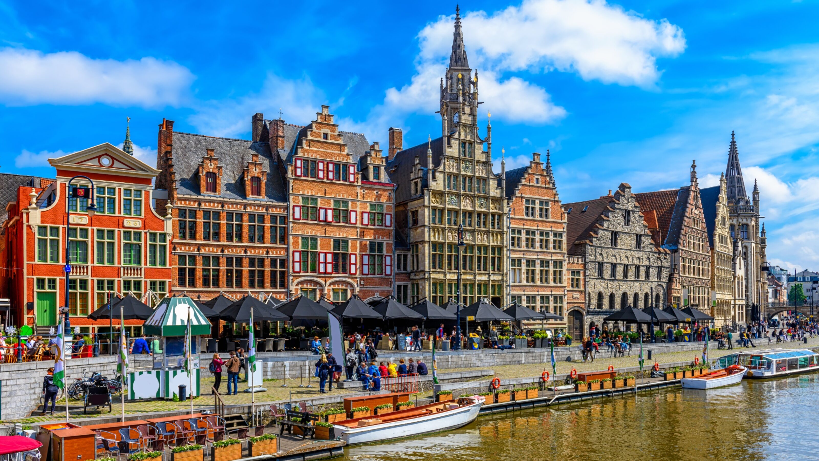 Colourful historic buildings by a canal with boats and people in Ghent, Belgium.