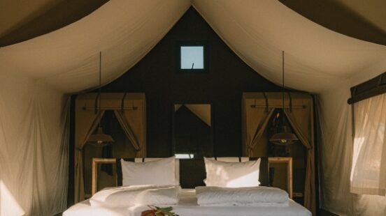 Cozy glamping tent interior with a bed, warm lighting, and rustic decor.